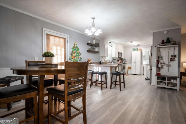 dining space featuring light wood-type flooring, an inviting chandelier, crown molding, and sink