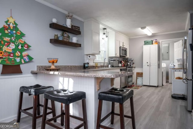 kitchen with white cabinets, light hardwood / wood-style flooring, appliances with stainless steel finishes, a kitchen bar, and kitchen peninsula