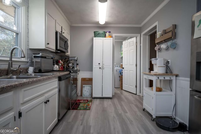 kitchen with sink, light hardwood / wood-style flooring, appliances with stainless steel finishes, white cabinets, and ornamental molding