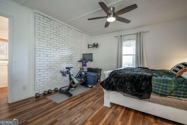 bedroom with ceiling fan, dark wood-type flooring, and brick wall