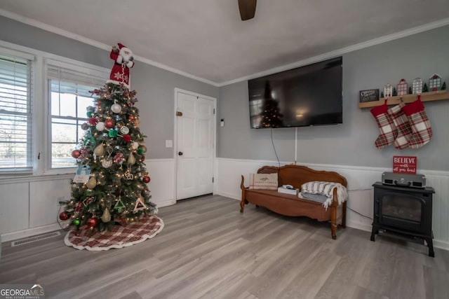 living area featuring a wood stove, light hardwood / wood-style flooring, ceiling fan, and ornamental molding