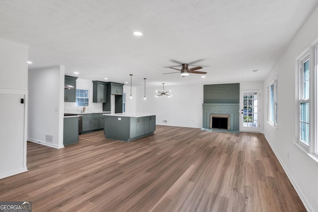 unfurnished living room featuring ceiling fan with notable chandelier, sink, a fireplace, a textured ceiling, and dark hardwood / wood-style flooring