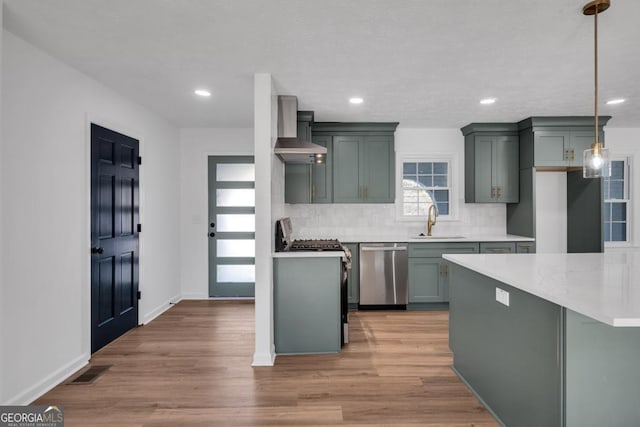 kitchen featuring tasteful backsplash, stainless steel appliances, wall chimney range hood, pendant lighting, and light hardwood / wood-style floors