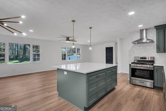 kitchen featuring a center island, wall chimney range hood, stainless steel gas range, decorative backsplash, and a textured ceiling