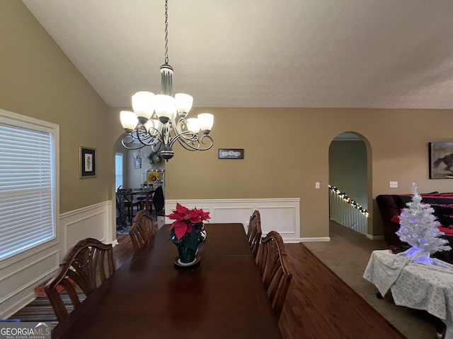 carpeted dining area featuring a textured ceiling, vaulted ceiling, and a notable chandelier