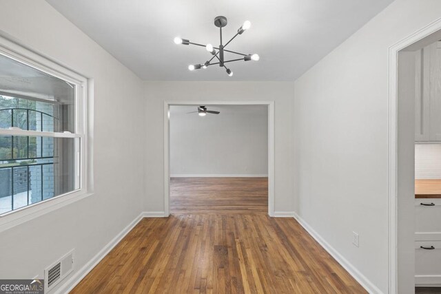 unfurnished dining area with ceiling fan with notable chandelier and dark hardwood / wood-style floors