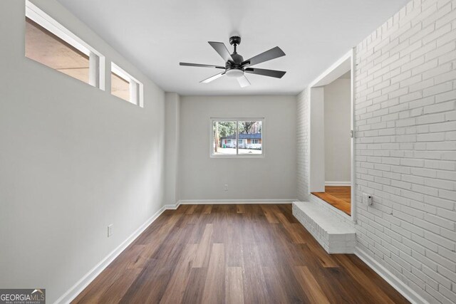 interior space with ceiling fan, dark hardwood / wood-style flooring, and brick wall