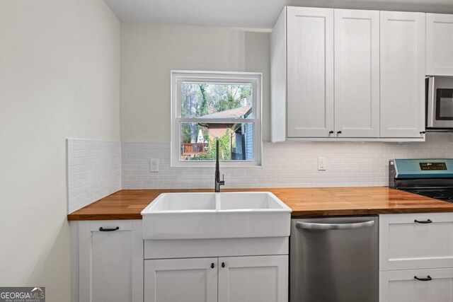 kitchen featuring white cabinets, stainless steel dishwasher, backsplash, and wooden counters