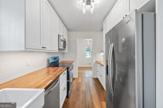 kitchen with decorative backsplash, appliances with stainless steel finishes, wood-type flooring, white cabinets, and butcher block countertops