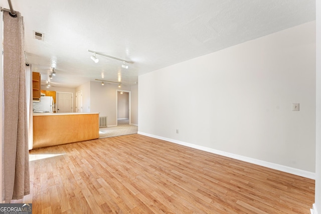 unfurnished living room featuring track lighting, a textured ceiling, and light hardwood / wood-style flooring