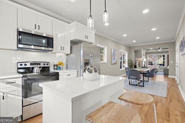 kitchen featuring a center island, white cabinets, hanging light fixtures, light wood-type flooring, and stainless steel appliances