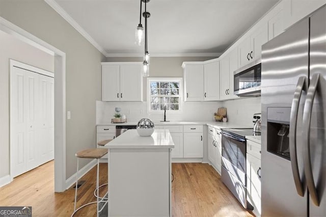 kitchen with stainless steel appliances, decorative light fixtures, white cabinets, light hardwood / wood-style floors, and a kitchen island