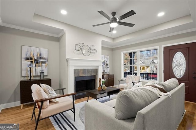 living room with a fireplace, hardwood / wood-style floors, a tray ceiling, and ceiling fan