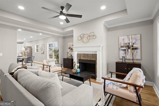 living room featuring hardwood / wood-style floors, ceiling fan, ornamental molding, and a tiled fireplace