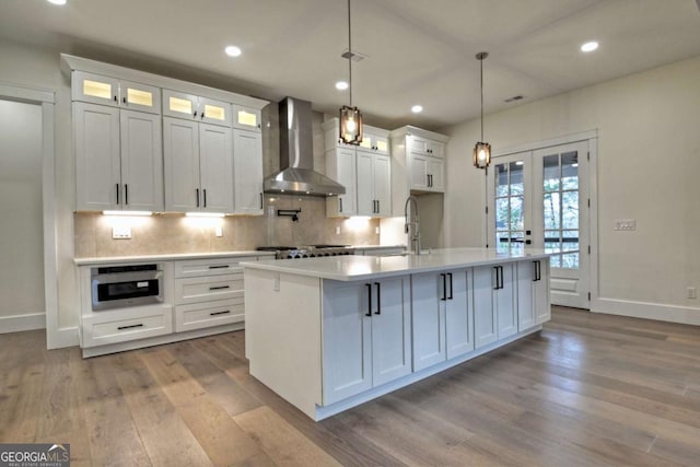 kitchen with a sink, wall chimney range hood, wood finished floors, white cabinetry, and light countertops