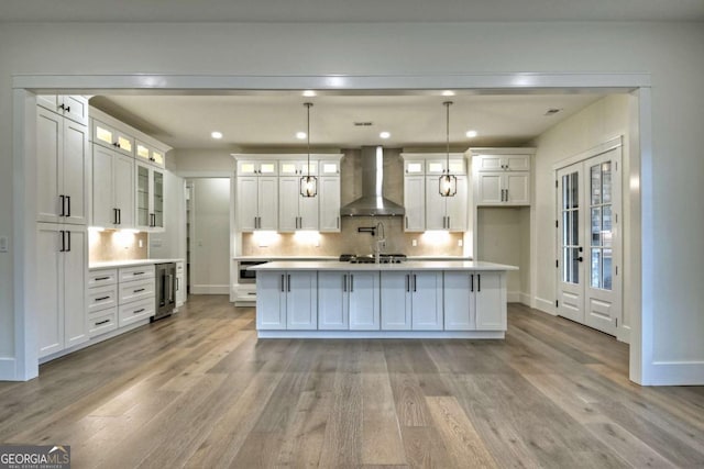 kitchen with white cabinets, light wood-type flooring, light countertops, and wall chimney range hood