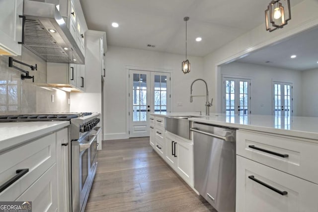 kitchen featuring light wood-type flooring, french doors, stainless steel appliances, and wall chimney exhaust hood