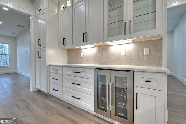 kitchen featuring decorative backsplash, beverage cooler, baseboards, and light wood finished floors