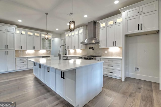 kitchen featuring a large island, light wood-style flooring, a sink, wall chimney exhaust hood, and light countertops