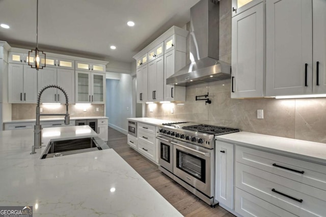 kitchen with decorative backsplash, wall chimney range hood, range with two ovens, and a sink