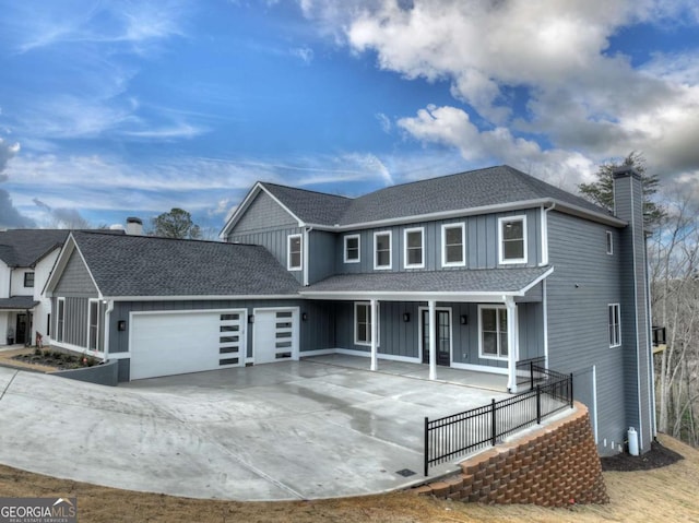 traditional-style home with driveway, a porch, board and batten siding, an attached garage, and a chimney