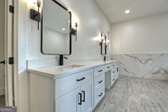 bathroom featuring double vanity, wainscoting, wood finished floors, tile walls, and a sink