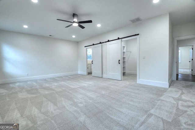 unfurnished bedroom featuring visible vents, baseboards, a barn door, light carpet, and recessed lighting