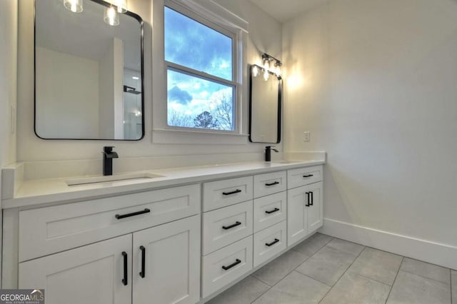 full bath with tile patterned flooring, double vanity, baseboards, and a sink