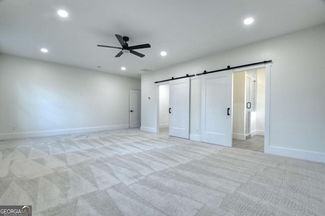 unfurnished bedroom with a barn door, recessed lighting, baseboards, and light carpet