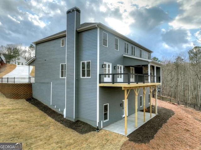 rear view of property featuring a balcony, fence, a yard, a chimney, and a patio area