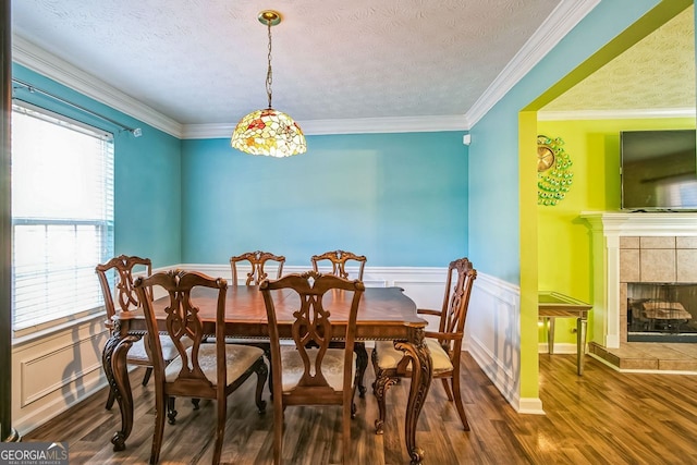 dining area with a healthy amount of sunlight, a tiled fireplace, crown molding, and dark wood-type flooring