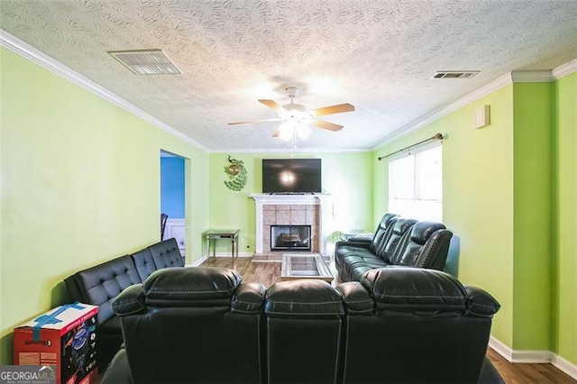 living room featuring a tile fireplace, hardwood / wood-style floors, a textured ceiling, and ornamental molding