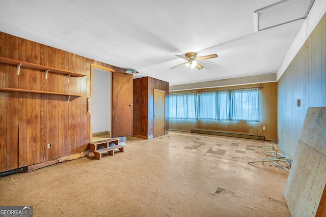 unfurnished living room with ceiling fan, a baseboard radiator, and wood walls