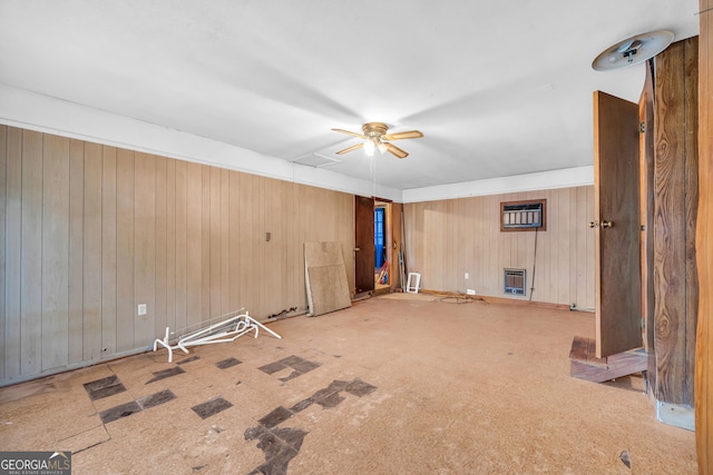 spare room with heating unit, wooden walls, ceiling fan, and light carpet