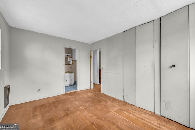 unfurnished bedroom featuring light wood-type flooring, a textured ceiling, and connected bathroom