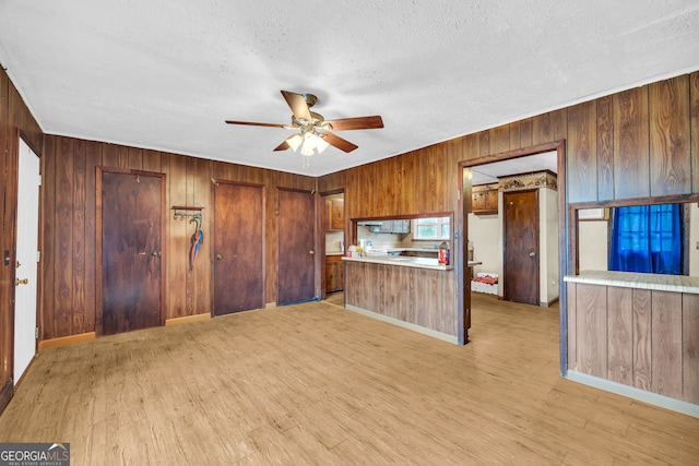 kitchen featuring kitchen peninsula, a textured ceiling, ceiling fan, wooden walls, and light hardwood / wood-style floors