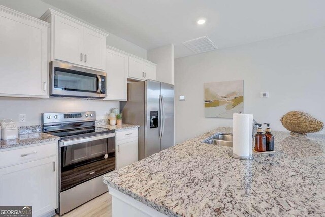 kitchen featuring light stone countertops, white cabinetry, appliances with stainless steel finishes, and light hardwood / wood-style flooring