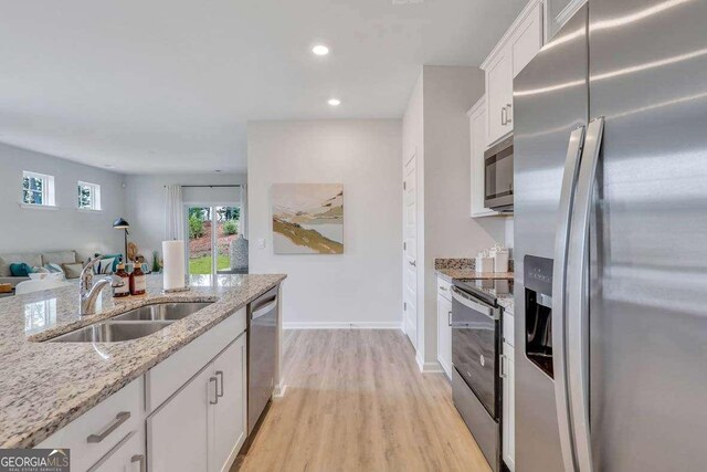 kitchen with light stone countertops, sink, stainless steel appliances, light hardwood / wood-style flooring, and white cabinets