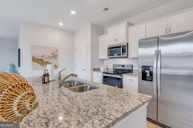 kitchen with light stone countertops, sink, stainless steel appliances, kitchen peninsula, and white cabinets