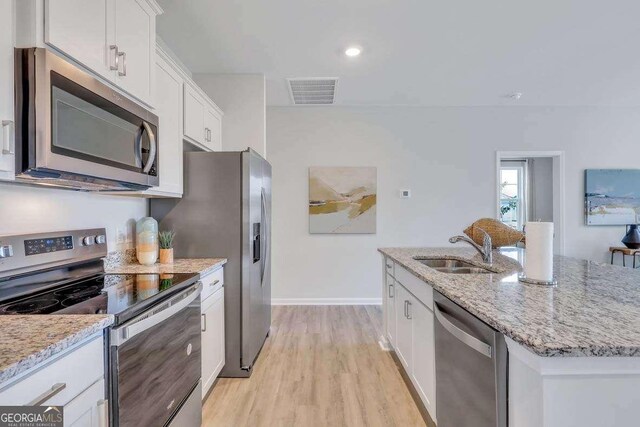 kitchen with sink, an island with sink, appliances with stainless steel finishes, light hardwood / wood-style floors, and white cabinetry