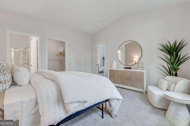 bedroom featuring a spacious closet, ensuite bathroom, vaulted ceiling, a closet, and carpet