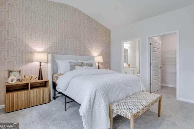 carpeted bedroom with a walk in closet, ensuite bathroom, and vaulted ceiling