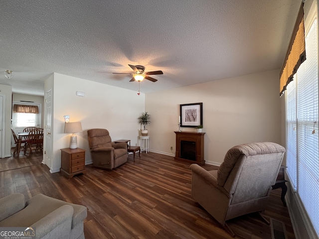 living room featuring dark wood-type flooring, ceiling fan, and a textured ceiling