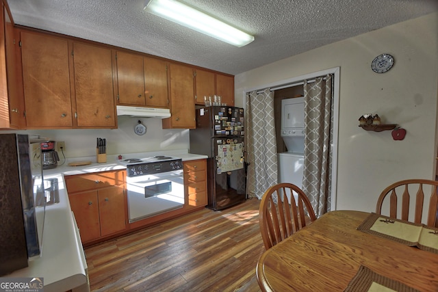 kitchen with black fridge, a textured ceiling, dark hardwood / wood-style floors, stacked washer / dryer, and oven