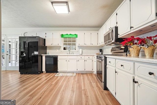 kitchen with decorative backsplash, white cabinetry, black appliances, and light hardwood / wood-style floors