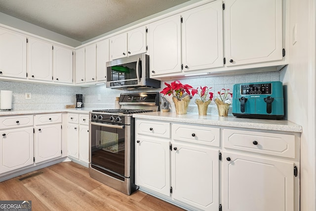 kitchen with white cabinetry, tasteful backsplash, a textured ceiling, appliances with stainless steel finishes, and light wood-type flooring