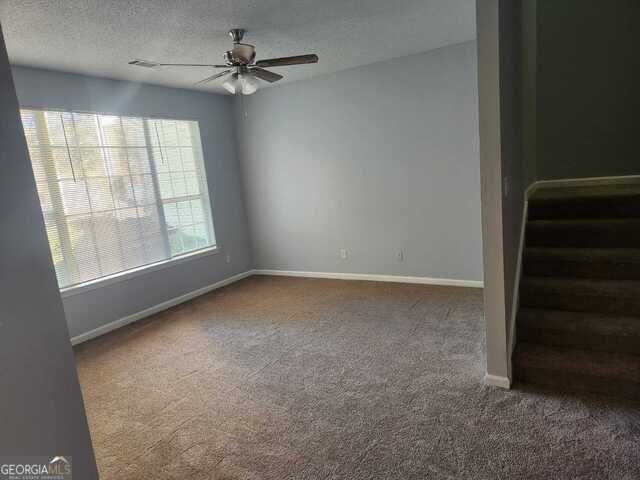 carpeted empty room with ceiling fan and a textured ceiling