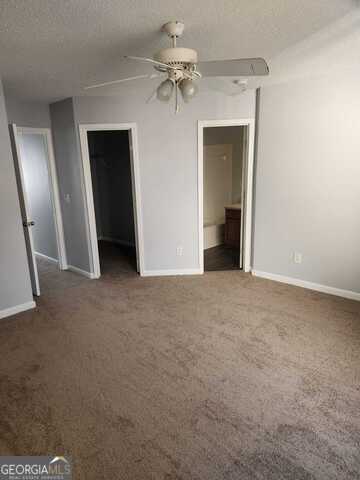 spare room with a textured ceiling, dark carpet, and ceiling fan