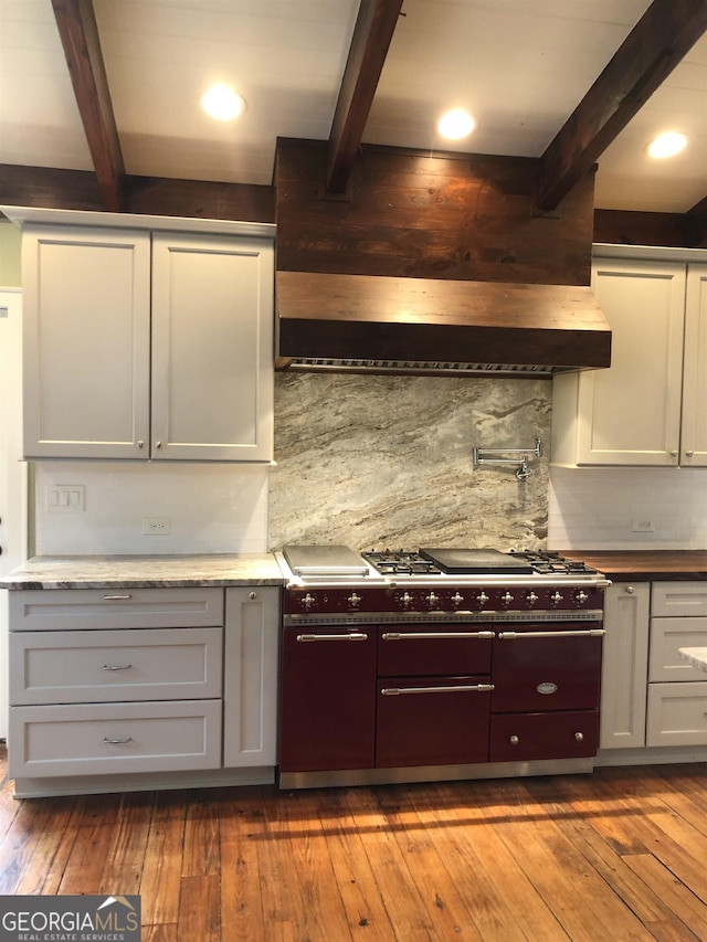 kitchen with wall chimney range hood, beam ceiling, wood-type flooring, and tasteful backsplash