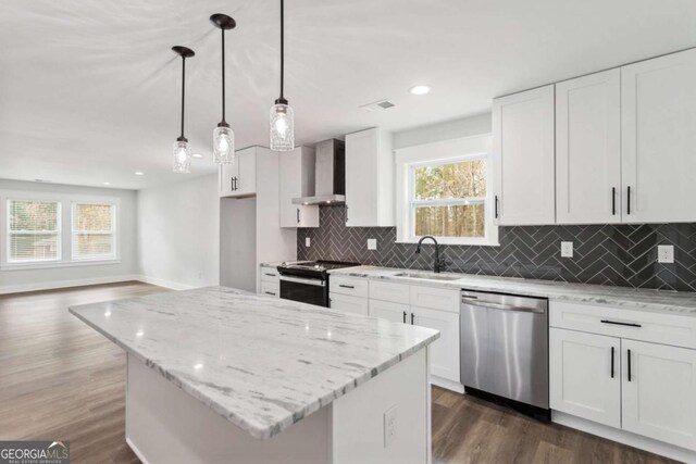 kitchen featuring light stone countertops, stainless steel appliances, wall chimney range hood, white cabinetry, and a sink